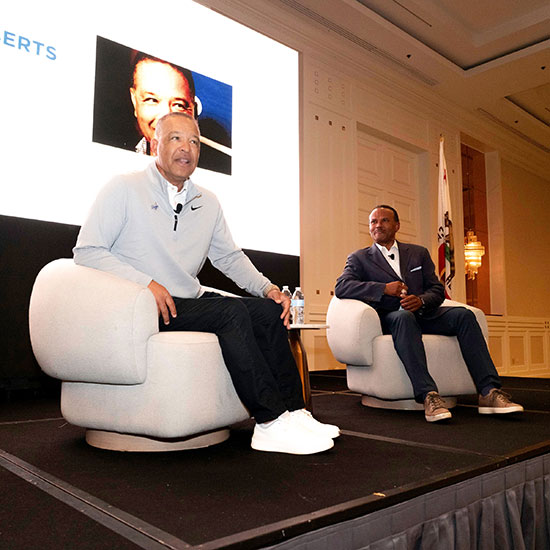 GLANCDA 2026 Member Luncheon & Annual Meeting; Two men sit in armchairs on a stage, engaged in conversation. A large screen behind shows a partial portrait photo. The setting is formal and professional.