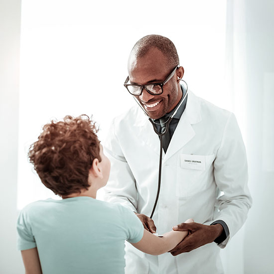 Ask Alison: Has Your Dealership Considered a Medical Captive? Doctor in a white coat smiles warmly at a child wearing a light blue shirt. The doctor gently holds the child's hand, creating a comforting atmosphere.