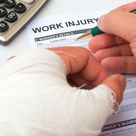 Workers’ Compensation, Experience-Modifier, and How Litigation Is Adding to Your Claims; A bandaged hand holds a pen, filling out a "Work Injury" form. A calculator is visible nearby. The setting conveys a sense of urgency and focus.